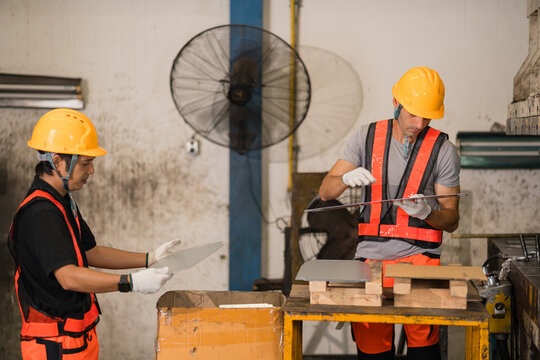 Two factory workers in orange safety vests examining sheet metal panel at workbench