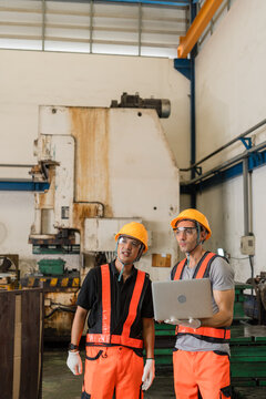 Two engineers discussing maintenance data on laptop before rusted mechanical stamping press vertical