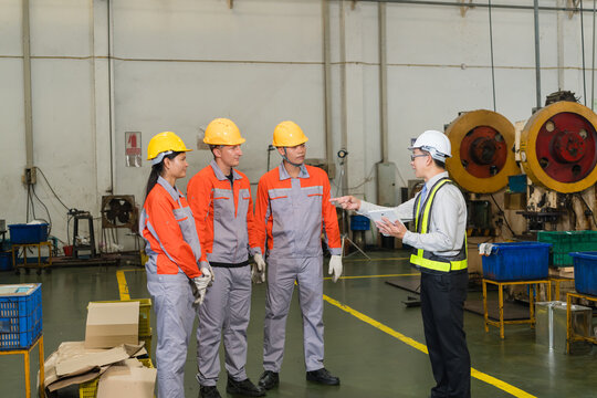 Engineer pointing while briefing coverall clad workers beside heavy duty stamping press machinery