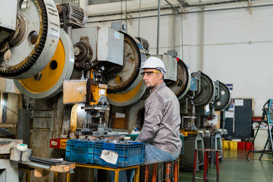 Machine operator turning toward camera during pause at metal stamping press