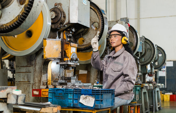Female Machine Operator Inspecting Stamped Metal Part Beside Industrial Power Press