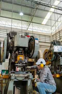 Wide View Of Machine Operator Kneeling Beside Tall Power Press Under Skylights