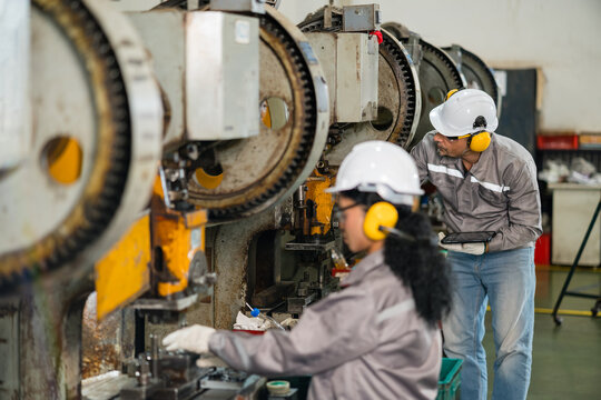 Two factory engineers inspecting a row of power press gears together with a tablet