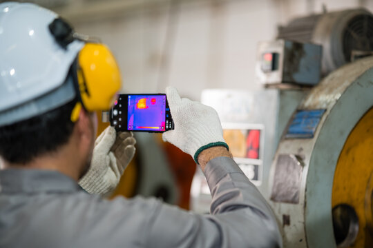 Engineer capturing thermal camera image of press machine motor during maintenance inspection