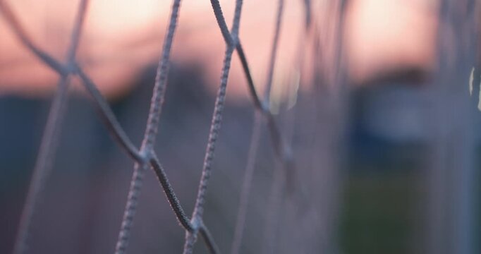 cinematic close-up of a football goal net during sunset with shallow depth of field and soft bokeh on an outdoor soccer field. The detailed texture of the net is sharply focused while the stadium 