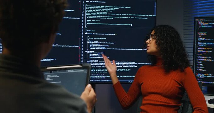 Hispanic man and woman programmers work together at night testing code debugging systems securing databases and collaborating on AI enabled applications in a modern workplace.