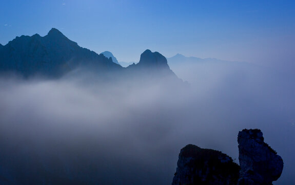 Mountain silhouettes emerge from thick twilight fog, showcasing a serene tourism destination for total nature exploration in the Julian Alps Natural Park, Alba Valley, Friuli Venezia Giulia, Italy...