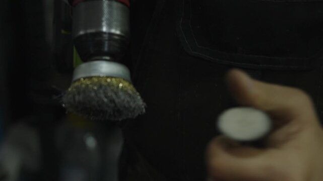 Close-up of mechanic cleaning metal part with rotating wire brush.