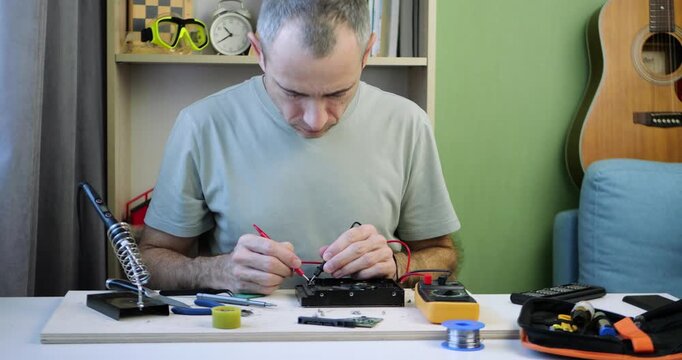 Man repairs electronic device at home using precision tools and technical skills. Hands-on electronics work highlights problem solving, diagnostics and modern DIY technology projects.