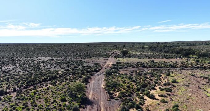 Scenic drone image overlooking the vast Great Karoo in South Africa's Western Cape. A rough farm track crosses a seasonal watercourse, highlighting the region's rugged beauty.