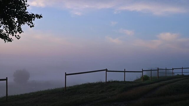 Mysterious foggy landscape during an early morning sunrise with thick haze over fields, peaceful seasonal weather