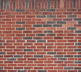 Fototapeta premium Close up of a red brick wall surface with scattered black bricks, variegated bricks and porous even mortar with a vertical top row of bricks 