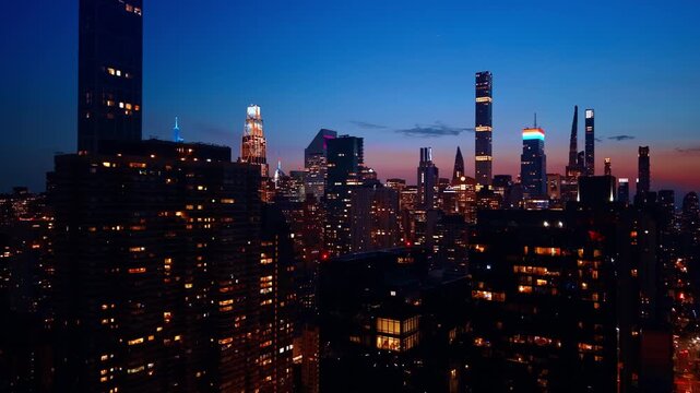 Dark high-rises with some lights in the windows. Tops of famous New York City skyscrapers against pink blue sky.