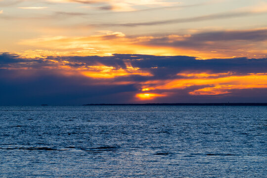 Sun sets behind dark clouds over deep blue sea. Beautiful orange sky with golden rays reflecting on water. Concept of hope and tranquility. Natural sunset background.