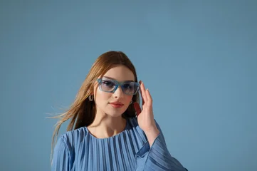 Beautiful fashionable woman wearing trendy blue color sunglasses, stylish pleated dress. Close up studio portrait. Copy, empty space for text © Victoria Fox