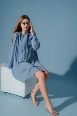 Beautiful fashionable woman wearing trendy blue color pleated short dress, sunglasses, silver metallic strap sandals. Full-length studio portrait. Copy, empty space for text © Victoria Fox