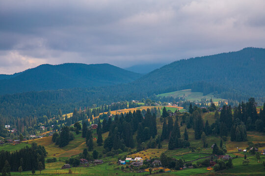 Picturesque mountain landscape. Ukrainian Carpathians. A cozy village lies in the valley below, surrounded by rolling green hills and misty mountain peaks. Bright traditional houses and untouched