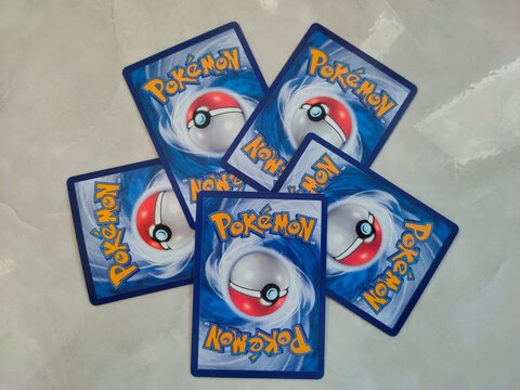 Malang, Indonesia - July 21, 2026: Five Pok&eacute;mon trading cards lie face down in a fanned arrangement on light marble, displaying their classic blue card backs.
