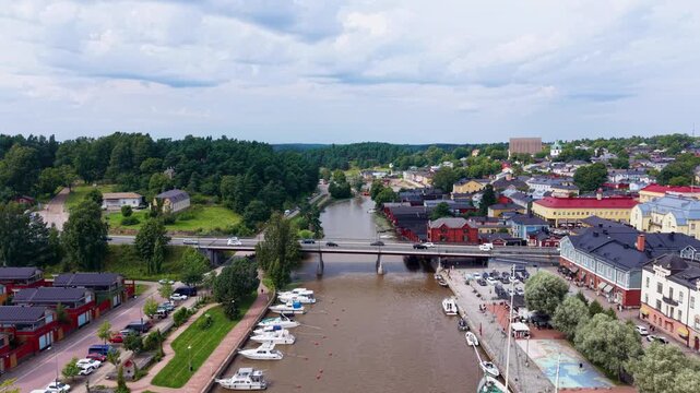 Aerial view over Porvoonjoki river toward Porvoo old town, showing colorful traditional wooden houses, road bridge, moored boats along the quay, and church tower, Finland