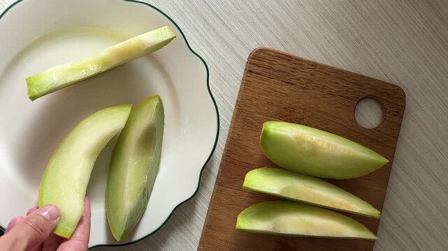 Hand picking a slice of fresh green melon from a wooden cutting board on white background