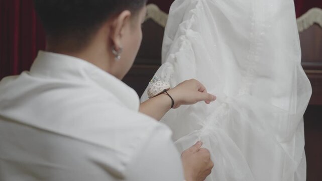 Fashion Designer Pulling Drawstring to Shape Wedding Dress Skirt During Couture Fitting