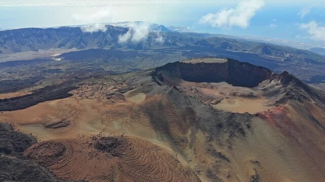 Aerial drone shot of Pico Viejo volcano on Tenerife, Canary Islands. The camera pushes in and pans right, revealing the dramatic volcanic landscape with rugged cliffs, crater, and the distant ocean.