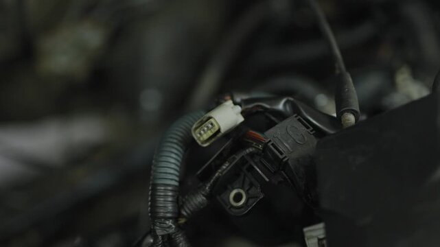 Unplugged plastic sensor connector plug hanging inside car engine bay.