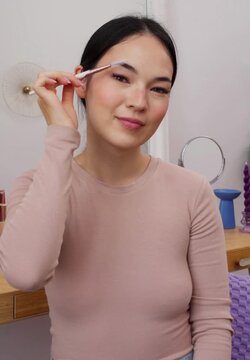 Smiling woman grooming eyebrows with spoolie brush during makeup routine