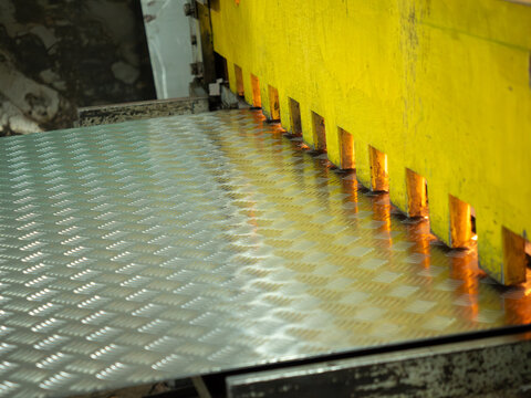 Industrial yellow hydraulic shear machine cutting shiny diamond pattern aluminum checker plate on factory workshop