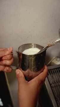 Milk frothing represents coffee culture, craftsmanship and professional beverage preparation. Hands steam milk with an espresso machine frother in a stainless steel pitcher for cappuccino or latte