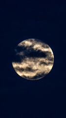 Full Moon Behind Dramatic Clouds in Night Sky Full moon partially covered by dramatic clouds against a dark blue night sky, creating a mysterious and atmospheric lunar scene. © Luis