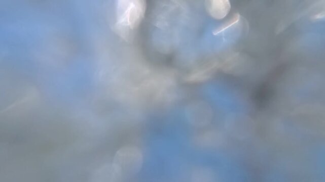 Horizontal HD 1080p super slow motion low angle shot of an outdoor metal shower head spraying refreshing water drops against a clear blue sky and green trees in summer