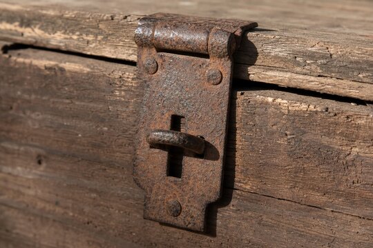 Close-up of a rusty iron hasp fastened on an old wooden crate with side lighting.