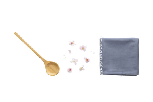 Minimalist wooden spoon with cherry blossom petals and blue linen napkin, organic kitchen utensils on white background, zen aesthetic culinary flat lay