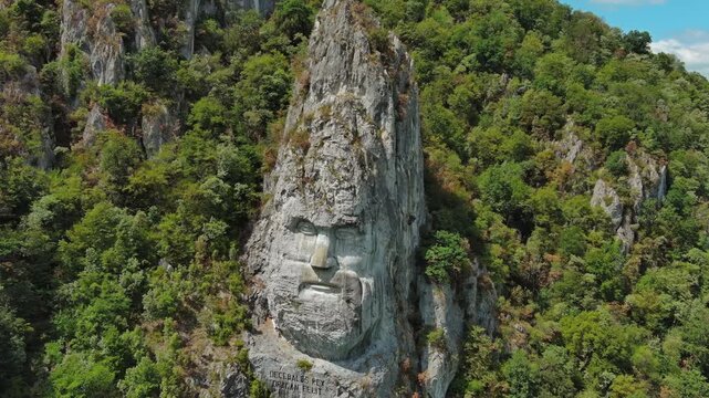 Aerial around view of stone carved statue portrait of ancient dacian king Decebal. Sculpture located on shore of Danube River, Romania, 4k