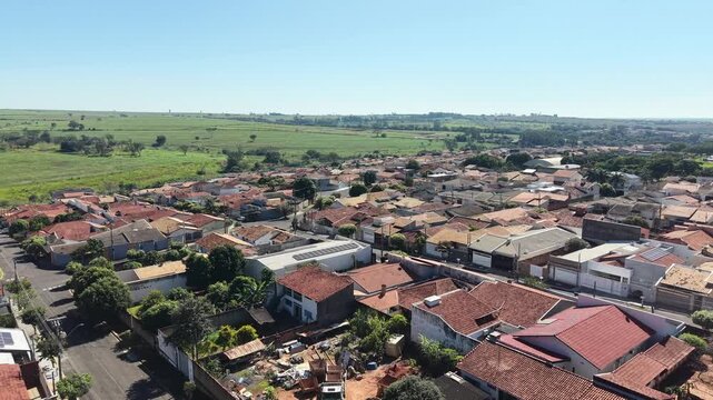 Aerial view of a residential neighborhood with red tiled roofs and green fields in the background under a clear blue sky