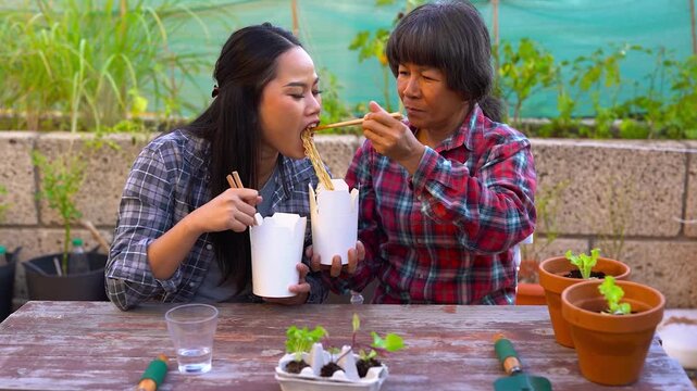 Happy asian mother and daughter eating together instant noodles at backyard - Thai family, food and lifestyle concept