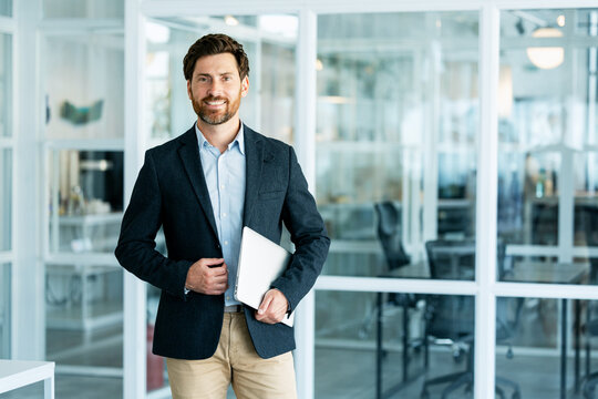 Smiling businessman holding laptop in modern office