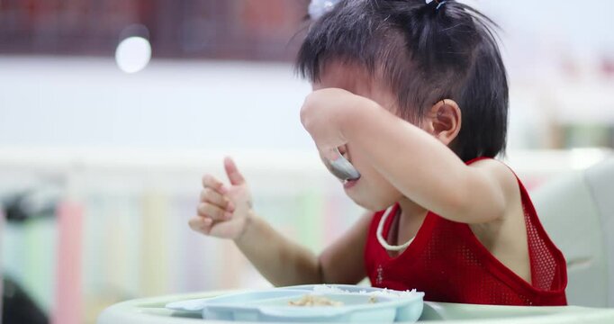 Asian left-handed toddler eating with a spoon independently, representing child development, self-feeding, healthy nutrition, left-handedness, and International Left-Handers Day