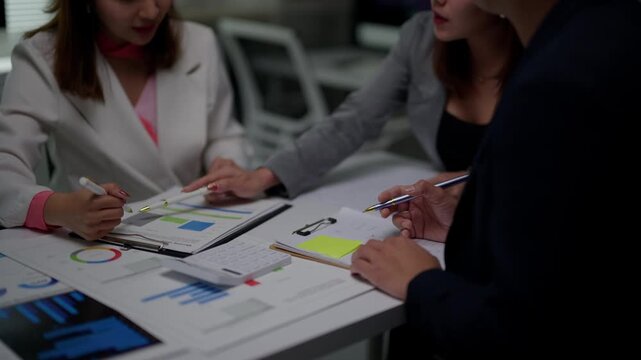 Business team analyzing data and planning strategy in a meeting, pointing at graphs and charts on financial reports while collaborating and brainstorming in the office