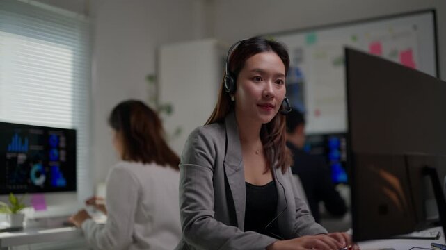 Asian call center operator wearing a headset working late at night, providing customer service and technical support to clients in a modern corporate office