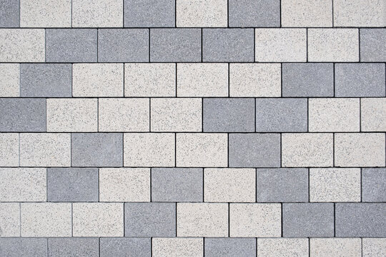 Rectangular concrete paving blocks form a clean geometric pattern. Light and dark grey stone tiles cover the walkway surface in top down