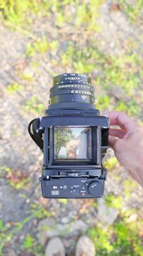 A man looks through the viewfinder of a vintage medium format camera. In the viewfinder, he sees the antique building on a sunny day