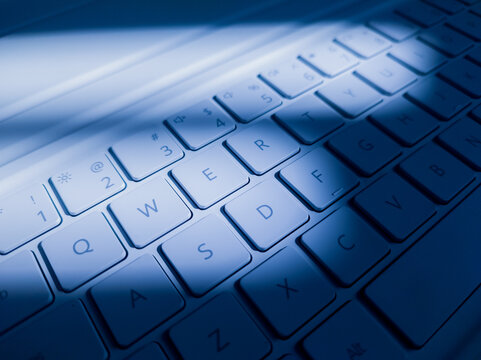 Modern white laptop QWERTY keyboard illuminated with cool blue light and dynamic shadows, representing modern technology, computing, typing, and digital work.