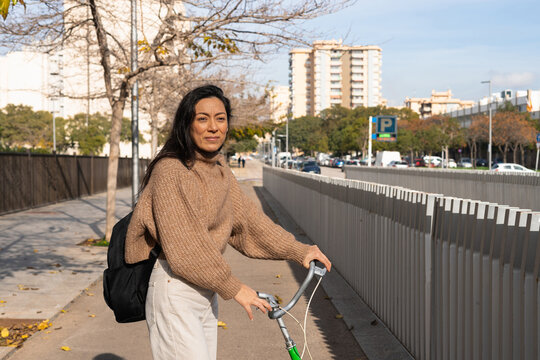 A happy woman looking around while holding a bicycle in the city
