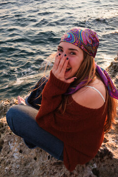 Young Woman Enjoys Time by the Sea and Smiles While Sitting on Rocks