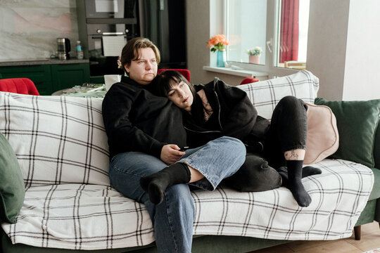 Two young women are watching TV on the couch at home.