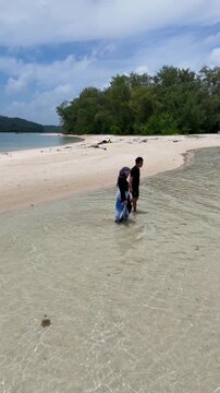 A couple walks along the white sandy beach at Kerayaan Beccu Beach and smiles at the camera