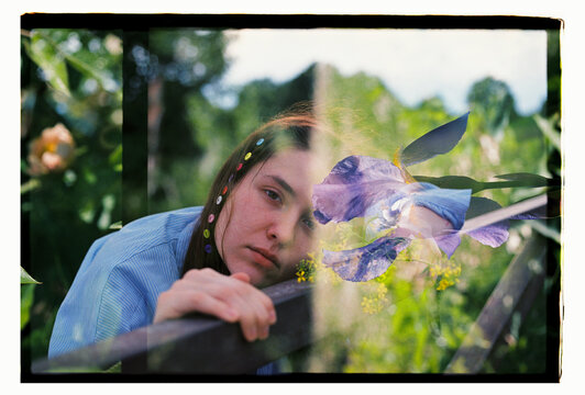 A young woman rests her chin on a garden fence among irises