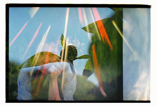 A double exposure merges hands, wildflowers, and tropical leaves